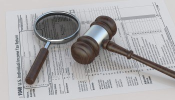 Magnifying glass and courtroom gavel laying on a tax law document.