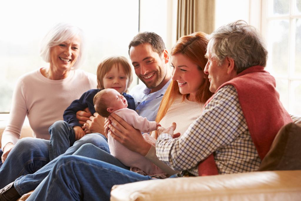 Multi Generation Family Sitting On Sofa With Newborn Baby